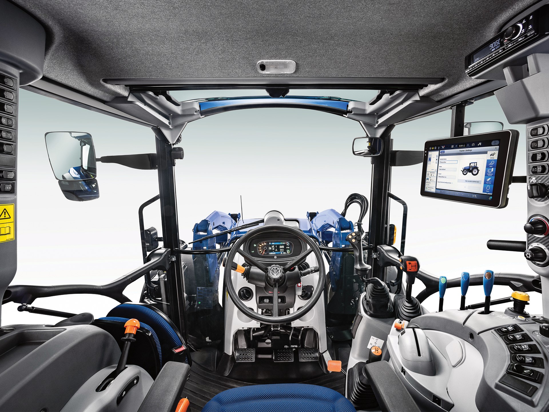 Interior view of a modern tractor cabin, featuring a steering wheel, control levers, and a digital display screen. The cabin is designed for operator comfort and efficiency, with ergonomic seating and various control buttons on the dashboard. Large side mirrors are visible, enhancing visibility for the driver.