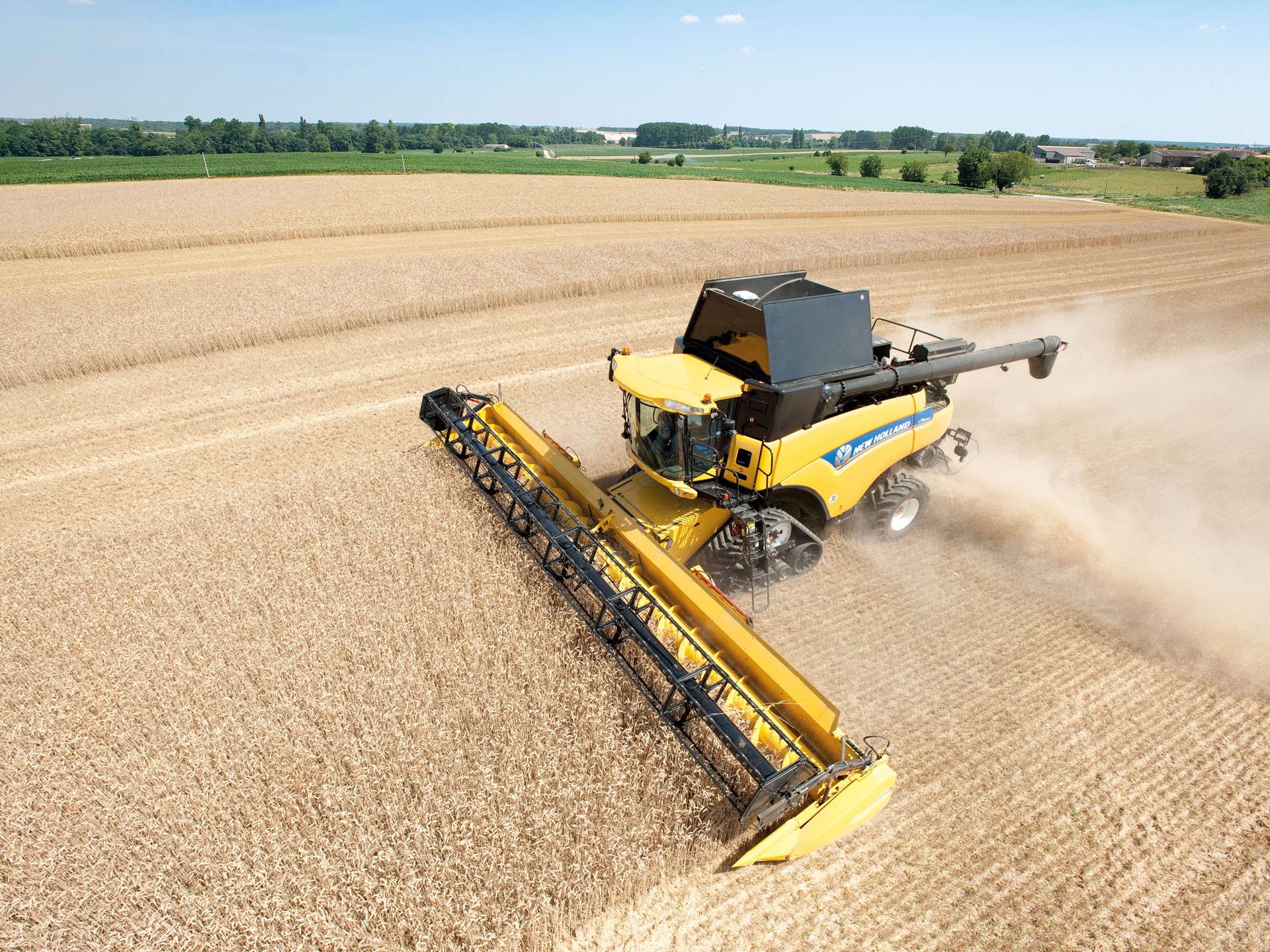 A yellow combine harvester working in a vast field of golden crops under a clear blue sky. Dust is being kicked up as the machine moves through the field, showcasing the agricultural landscape with green trees in the background.