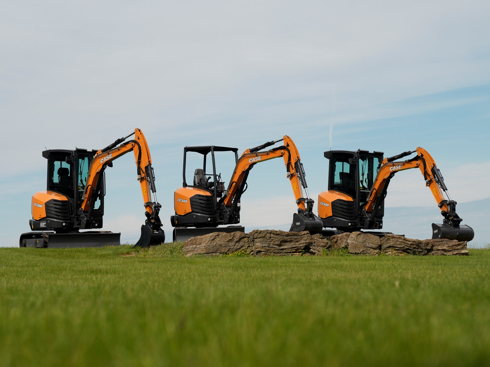 Three CASE mini excavators positioned on a grassy field with a clear sky background with their arms extended and buckets resting on the ground