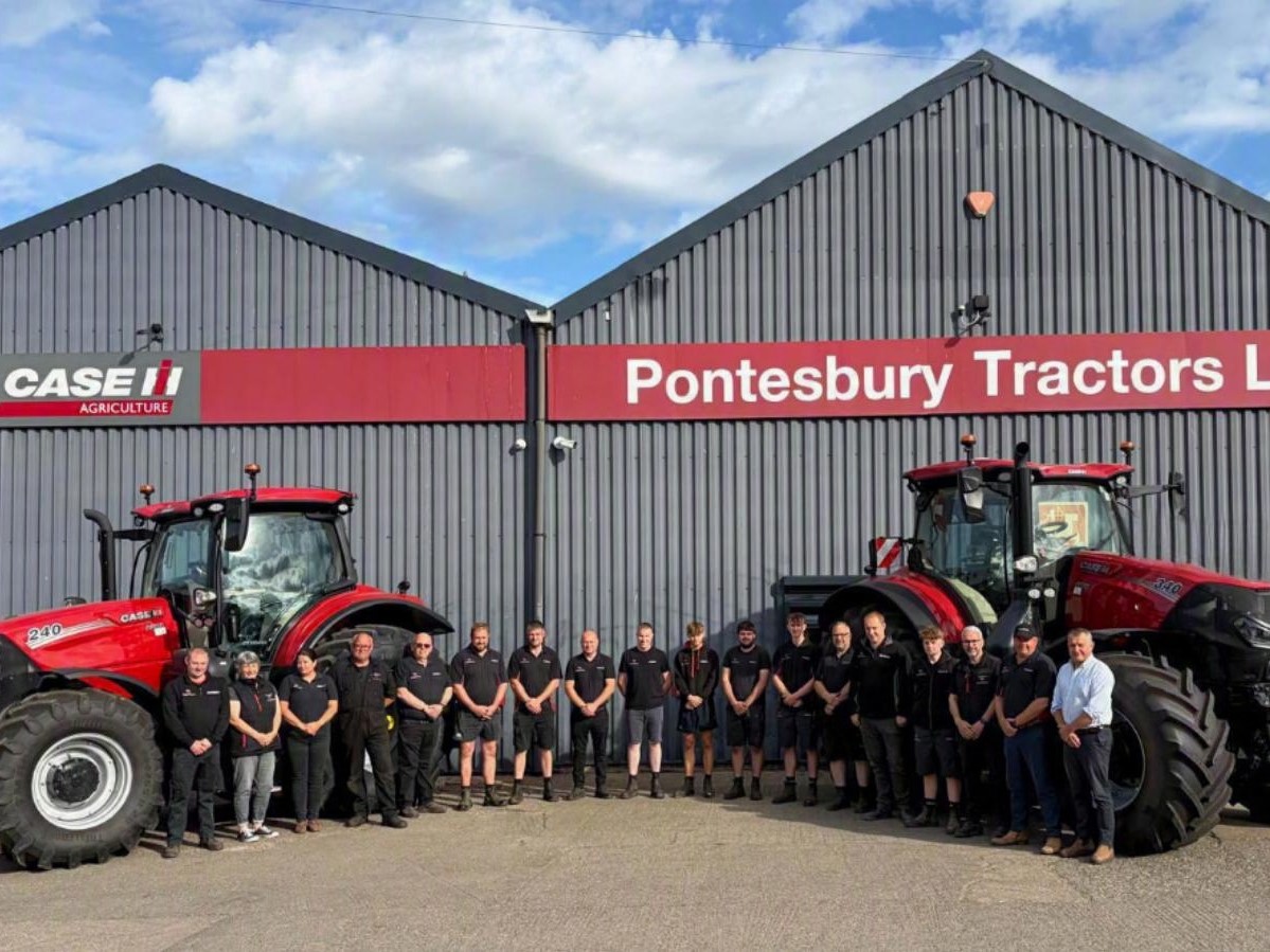 A group of people standing in front of two large red Case IH tractors outside a grey industrial building with red signage that reads "Pontesbury Tractors Ltd." under a partly cloudy blue sky.