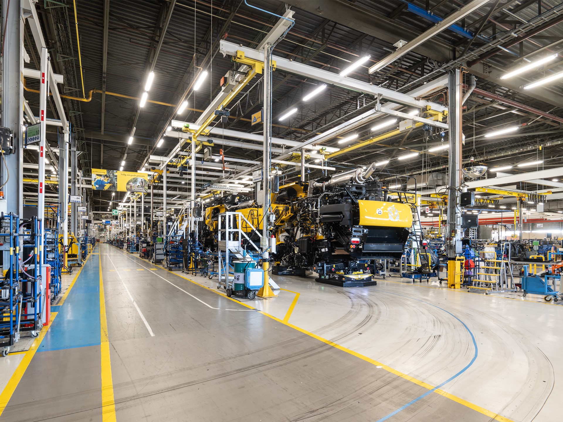 Interno di una grande fabbrica moderna con linee di assemblaggio di macchinari pesanti gialli, illuminazione a LED e pavimenti segnati per la sicurezza, senza operai visibili.