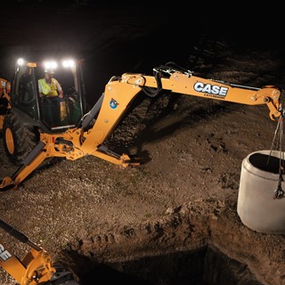 Backhoe winching a concrete pipe section into place at night