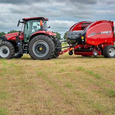 A red tractor attached to a red Case IH RB566 round baler parked on a grassy field under a cloudy sky, with trees and hay bales visible in the background.