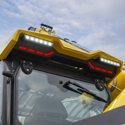 Close-up view of the front cabin of a yellow construction vehicle with bright LED lights and red accent lights on the roof, set against a partly cloudy sky background.