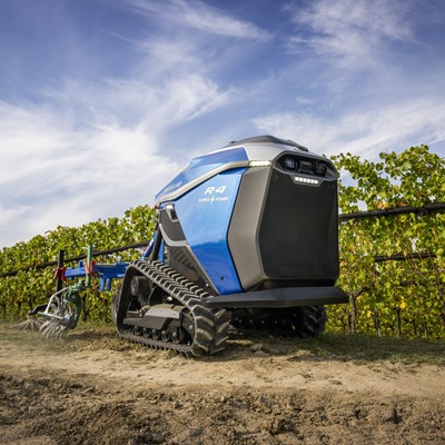 A blue autonomous agricultural robot with tank-like tracks working in a vineyard under a partly cloudy sky, equipped with farming tools for soil cultivation.