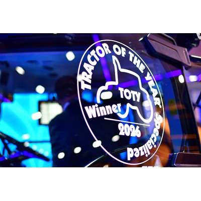 Close-up of a glass window on a tractor displaying a white decal that reads "TRACTOR OF THE YEAR Specialized Winner 2026 TOTY" with a tractor silhouette in the center, reflecting colorful blue and purple lights in the background.