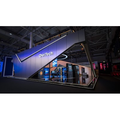 Modern exhibition booth for CNH Tech at a trade show, featuring a sleek angular design with illuminated edges, digital screens displaying technology-related content, and several people interacting inside the booth under a high-ceiling industrial venue.