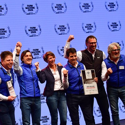 A group of eight people standing on stage celebrating an award at the Farm Machine 2026 event. Most of them are wearing blue vests and smiling, with some raising their fists in excitement. One person is holding a framed certificate that reads "New Holland Methane Power." The background features a repeated "Farm Machine 2026" logo.