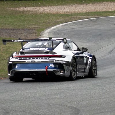 Rear view of a silver and black race car with the number 31 on the rear window and side, driving on a curved race track with grass on the left side.
