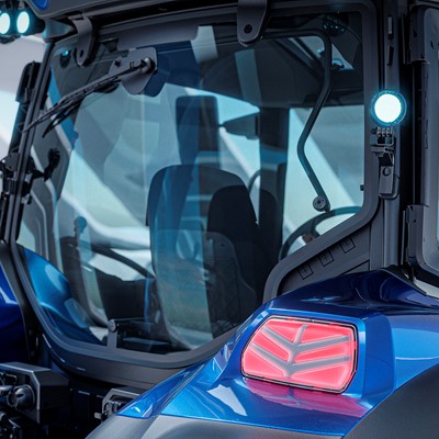 Close-up view of the rear section of a modern blue tractor with large black tires, illuminated rear lights, and a glass-enclosed cabin, set against a futuristic, well-lit background.