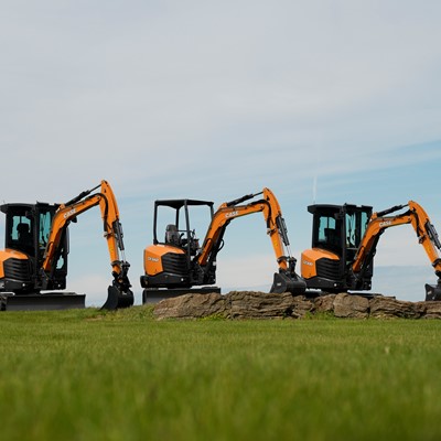 Three CASE mini excavators positioned on a grassy field with a clear sky background with their arms extended and buckets resting on the ground