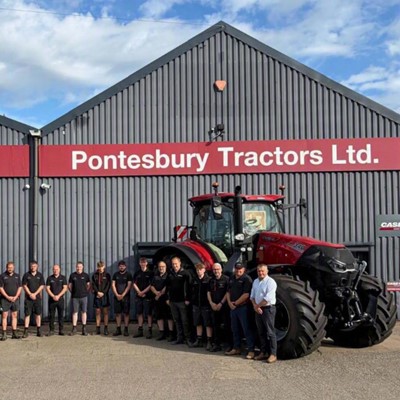 A group of people standing in front of two large red Case IH tractors outside a grey industrial building with red signage that reads "Pontesbury Tractors Ltd." under a partly cloudy blue sky.
