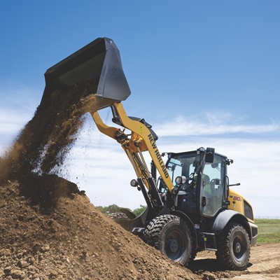A yellow New Holland wheel loader is dumping a load of dirt onto a large pile at a construction site under a clear blue sky.