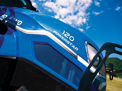Close-up view of a blue New Holland tractor with the model name "120 Powerstar" prominently displayed. The image captures the tractor's sleek design against a backdrop of a clear blue sky with scattered clouds, highlighting its modern features and agricultural utility.