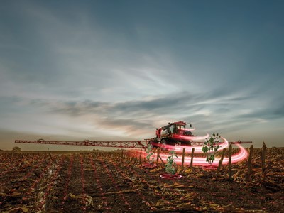 A modern agricultural sprayer is operating in a field at dusk, with a dramatic sky in the background. The sprayer is surrounded by swirling red light effects, emphasizing its motion as it applies treatment to the crops. The field is lined with rows of plants, showcasing a blend of technology and farming practices.