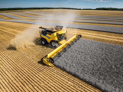 A yellow combine harvester is cutting through a field of golden crops, creating neat rows of harvested grain. The sky is clear with a few clouds, and the landscape features alternating stripes of harvested and unharvested fields, showcasing agricultural activity.