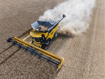 Aerial view of a yellow combine harvester working in a field, with dust and debris being kicked up as it cuts through rows of crops. The machine is equipped with a wide header, efficiently harvesting the agricultural produce. The surrounding field shows neatly arranged crop rows, highlighting the agricultural landscape.