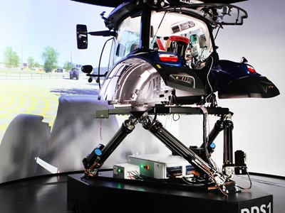 A high-tech driving simulator setup featuring a tractor cabin mounted on a multi-axis motion platform labeled "DDS1," with a large curved screen in the background displaying a virtual outdoor environment, designed for immersive agricultural machinery training or testing.