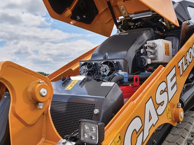 Close up view of the open engine compartment of a yellow CASE TL100EV electric mini track loader under a partly cloudy sky