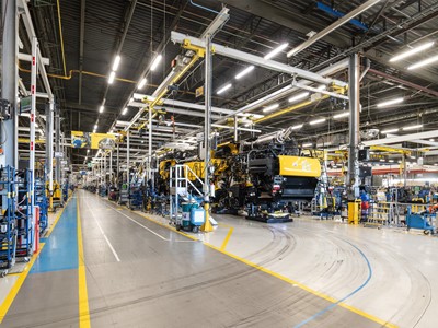 Interno di una grande fabbrica moderna con linee di assemblaggio di macchinari pesanti gialli, illuminazione a LED e pavimenti segnati per la sicurezza, senza operai visibili.