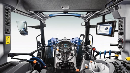 Interior view of a modern tractor cabin, featuring a steering wheel, control levers, and a digital display screen. The cabin is designed for operator comfort and efficiency, with ergonomic seating and various control buttons on the dashboard. Large side mirrors are visible, enhancing visibility for the driver.