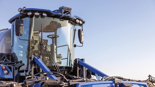 Close-up view of a modern blue agricultural tractor, showcasing its cab with large windows, advanced lighting, and various hydraulic components. The background features a clear blue sky, emphasizing the tractor's design and functionality for farming tasks.
