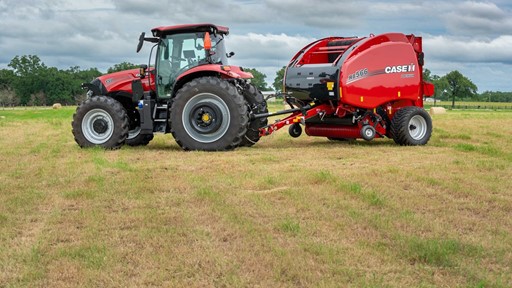 A red tractor attached to a red Case IH RB566 round baler parked on a grassy field under a cloudy sky, with trees and hay bales visible in the background.