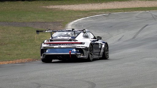 Rear view of a silver and black race car with the number 31 on the rear window and side, driving on a curved race track with grass on the left side.