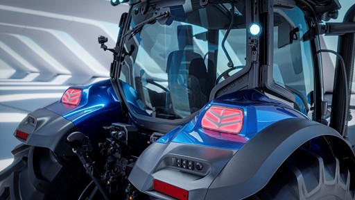 Close-up view of the rear section of a modern blue tractor with large black tires, illuminated rear lights, and a glass-enclosed cabin, set against a futuristic, well-lit background.