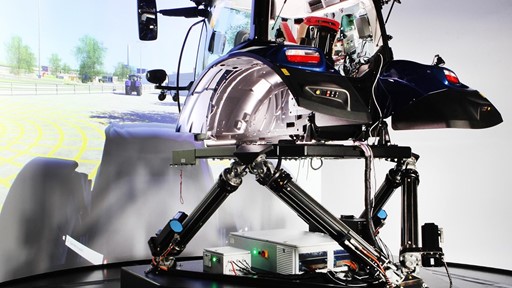 A high-tech driving simulator setup featuring a tractor cabin mounted on a multi-axis motion platform labeled "DDS1," with a large curved screen in the background displaying a virtual outdoor environment, designed for immersive agricultural machinery training or testing.