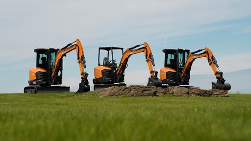 Three CASE mini excavators positioned on a grassy field with a clear sky background with their arms extended and buckets resting on the ground