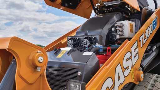 Close up view of the open engine compartment of a yellow CASE TL100EV electric mini track loader under a partly cloudy sky