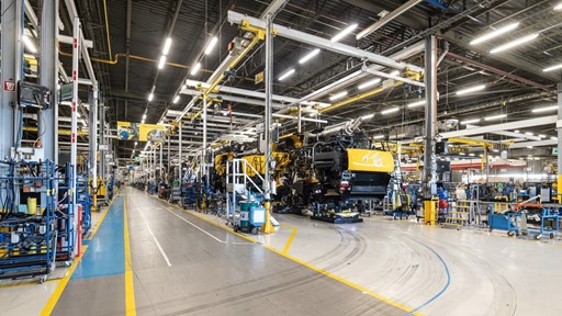 Interno di una grande fabbrica moderna con linee di assemblaggio di macchinari pesanti gialli, illuminazione a LED e pavimenti segnati per la sicurezza, senza operai visibili.