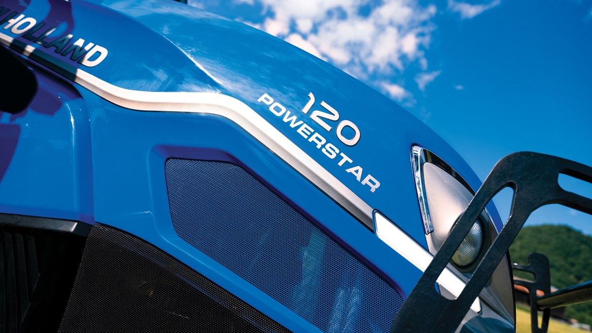 Close-up view of a blue New Holland tractor with the model name "120 Powerstar" prominently displayed. The image captures the tractor's sleek design against a backdrop of a clear blue sky with scattered clouds, highlighting its modern features and agricultural utility.