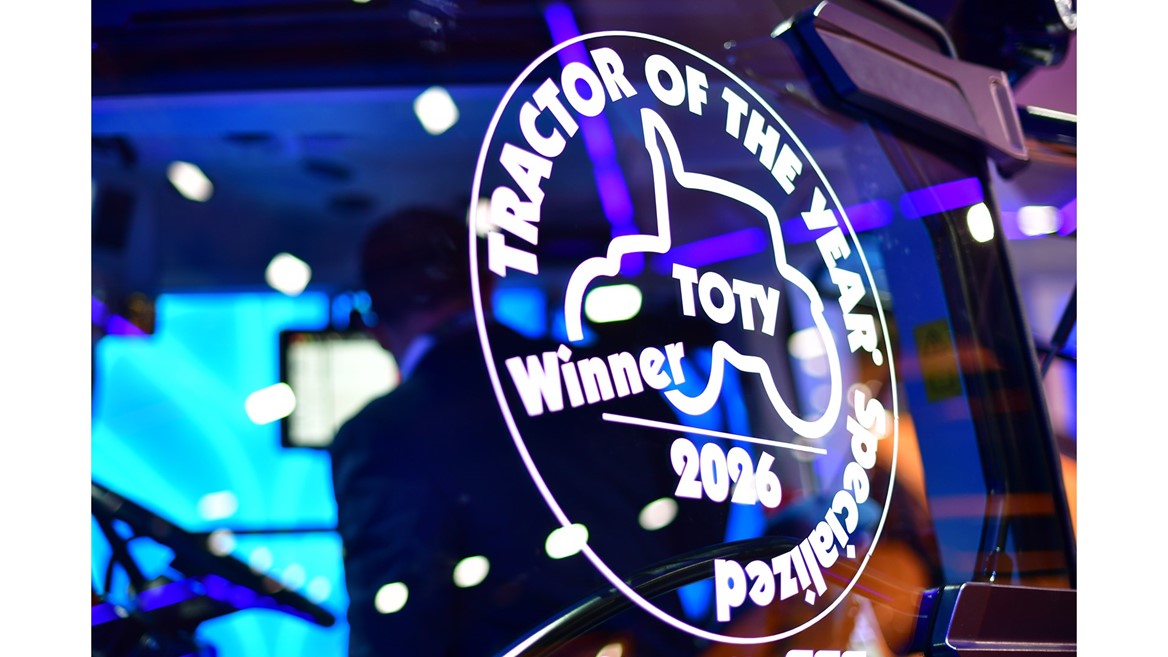 Close-up of a glass window on a tractor displaying a white decal that reads "TRACTOR OF THE YEAR Specialized Winner 2026 TOTY" with a tractor silhouette in the center, reflecting colorful blue and purple lights in the background.