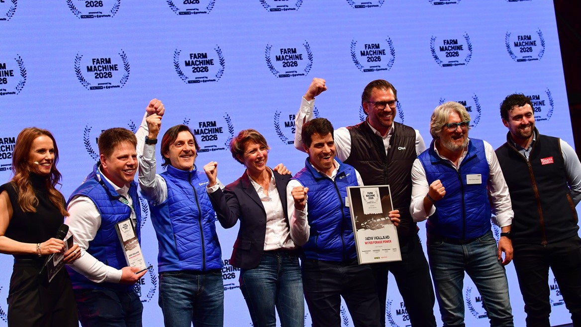 A group of eight people standing on stage celebrating an award at the Farm Machine 2026 event. Most of them are wearing blue vests and smiling, with some raising their fists in excitement. One person is holding a framed certificate that reads "New Holland Methane Power." The background features a repeated "Farm Machine 2026" logo.