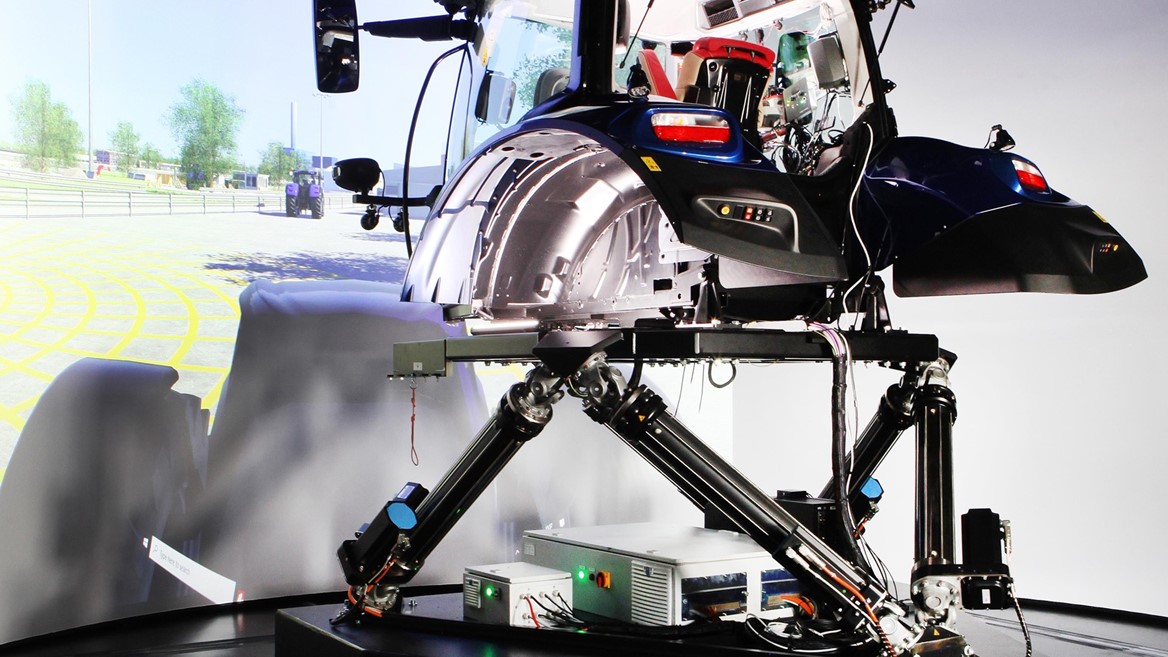 A high-tech driving simulator setup featuring a tractor cabin mounted on a multi-axis motion platform labeled "DDS1," with a large curved screen in the background displaying a virtual outdoor environment, designed for immersive agricultural machinery training or testing.