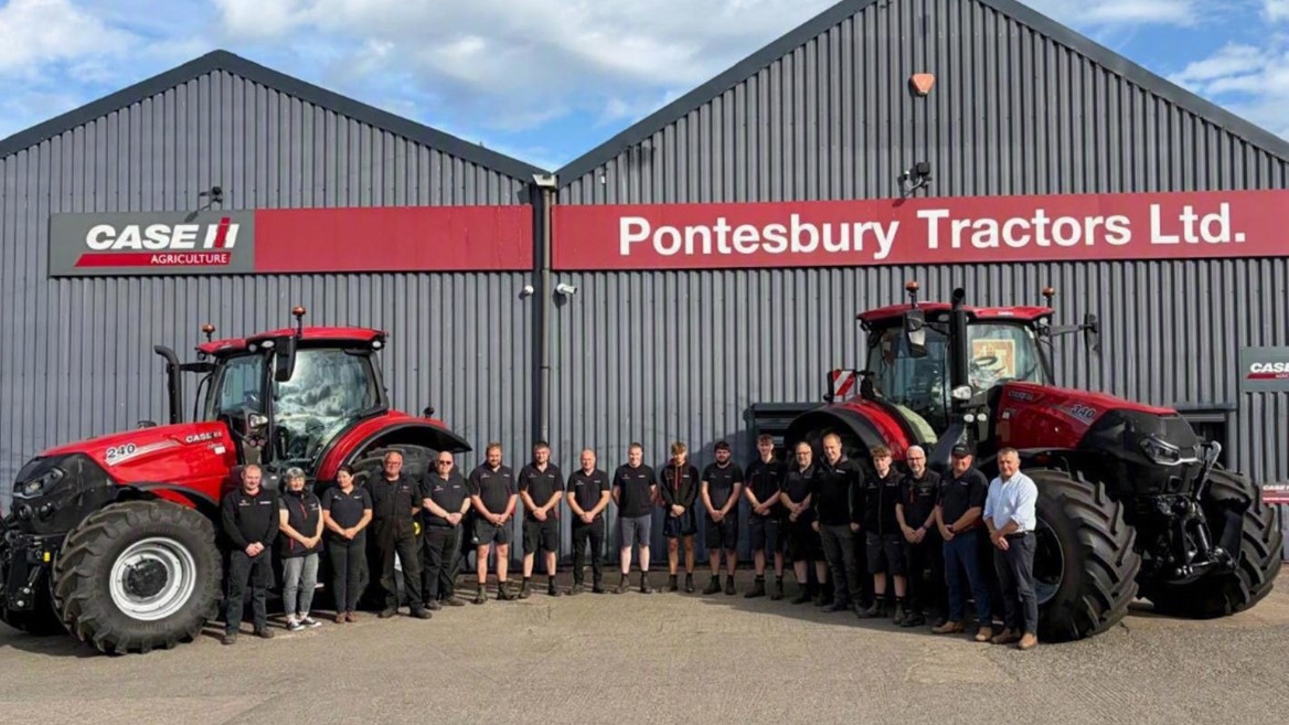 A group of people standing in front of two large red Case IH tractors outside a grey industrial building with red signage that reads "Pontesbury Tractors Ltd." under a partly cloudy blue sky.
