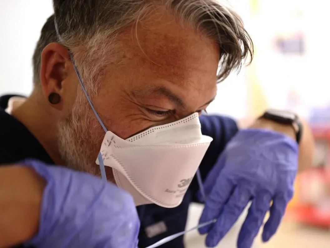 Nurse Jason Doff carefully removes his N95 mask after emerging from a room in the acute care COVID 19 unit at the Harbo