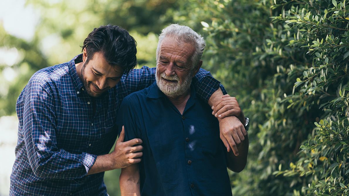 Young man with arm over shoulder of older man outdoors