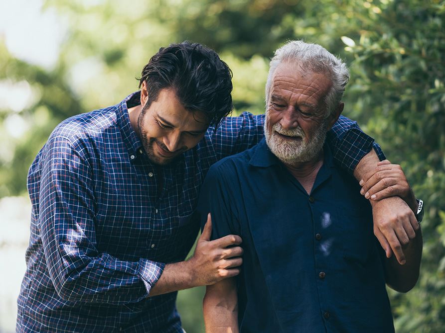 Young man with arm over shoulder of older man outdoors