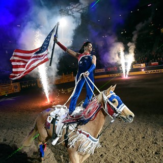 A rider carries the American flag during the opening ceremonies at the start of the seventh go-round of the NFR