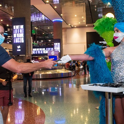 Las Vegas Showgirl hands an arriving visitor a mask at McCarran International Airport June, 26, 2020