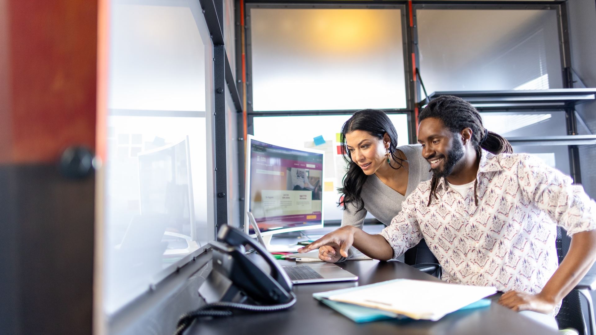 Two people collaborate in a modern workspace exploring solutions on a computer screen