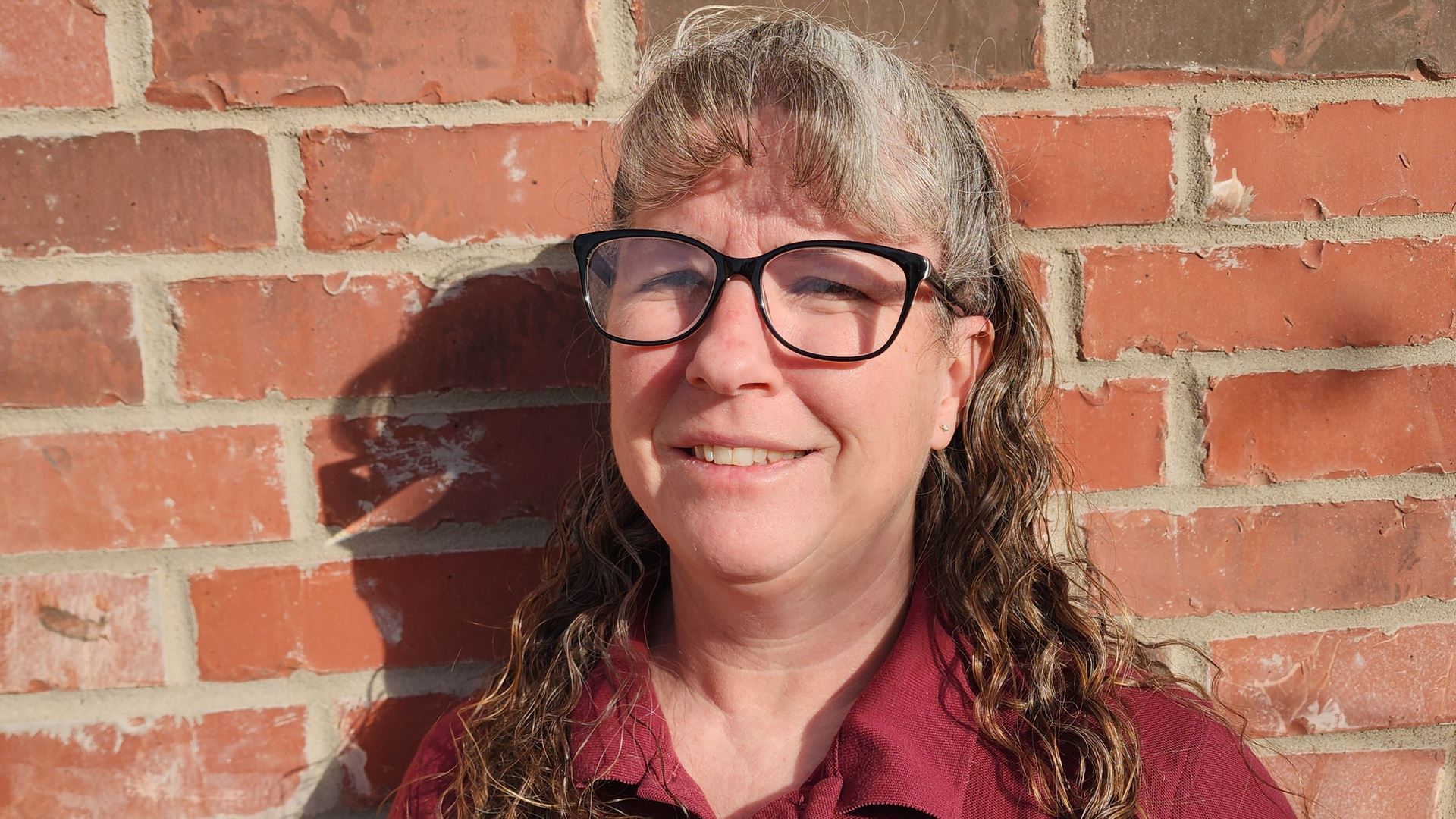 Head and shoulders of a woman standing next to a brick wall