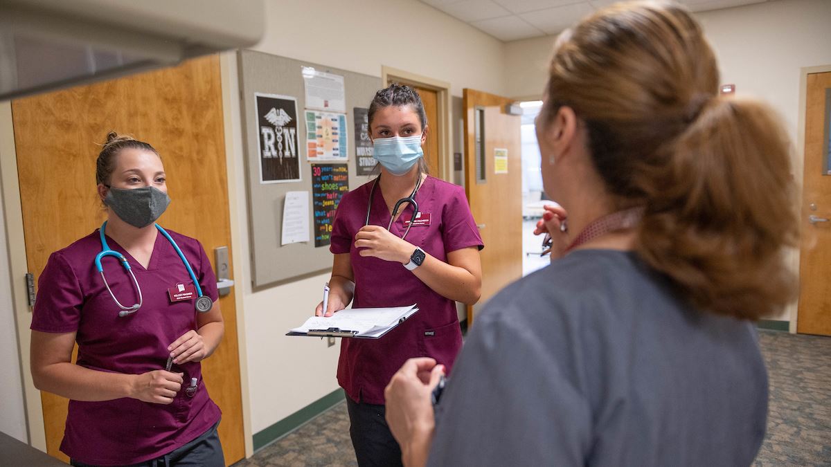 IMAGE DESCRIPTION Two nursing students speaking with a professor