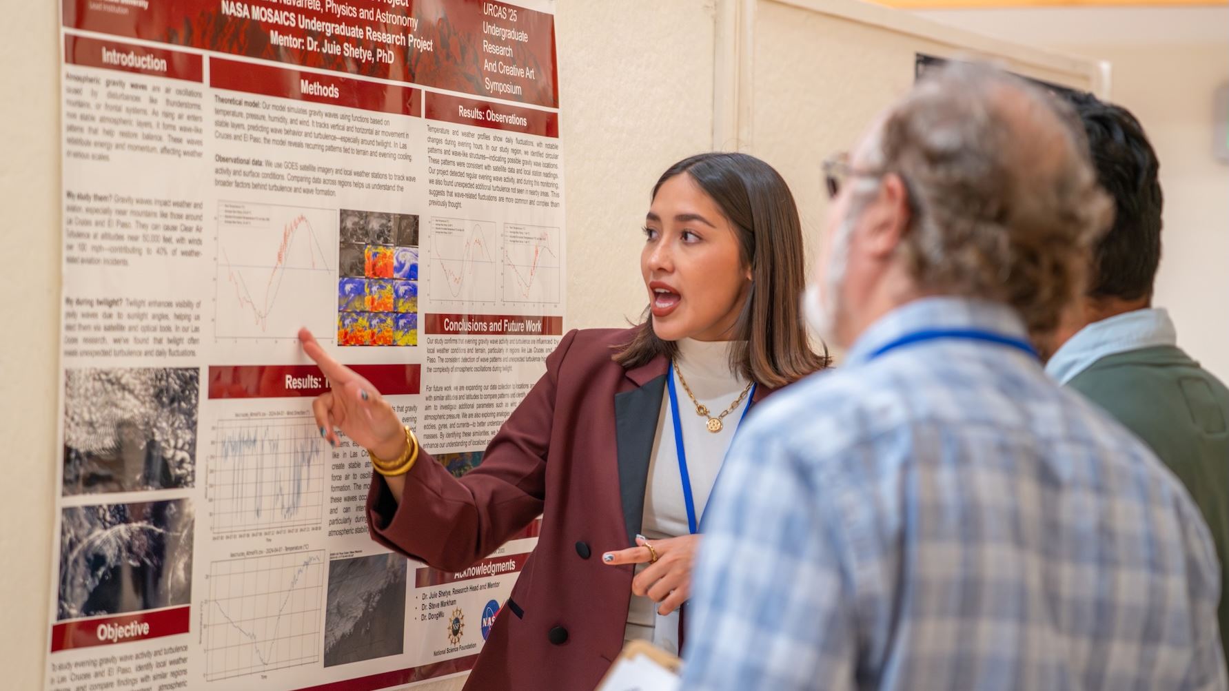 DESCRIPTION A girl points at a research poster with text and graphics while two people watch her