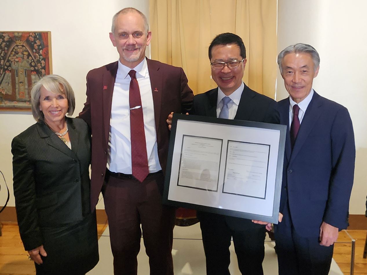 Four people pose with a framed document From left to right New Mexico Gov Michelle Lujan Grisham NMSU President Valerio Ferme Fujitsu Vice President Yoichi Murakami and Japanese Ambassador to the U S Shigeo Yamada