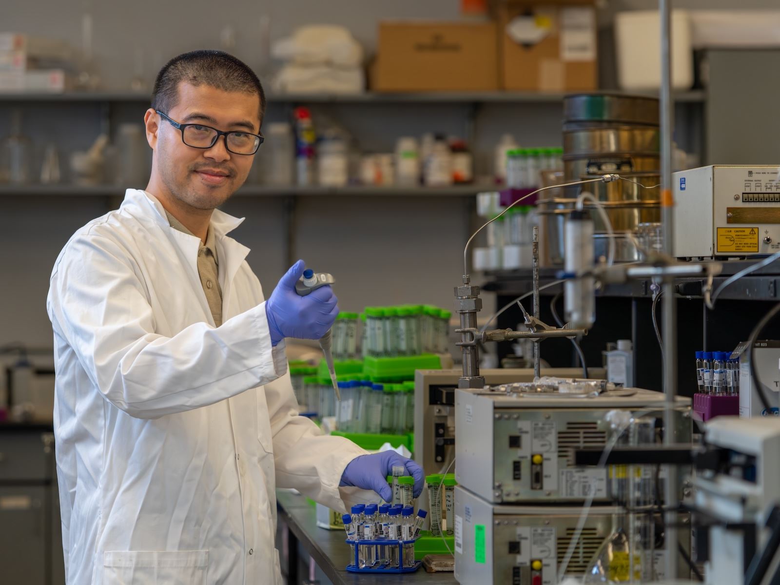 A man in a lab coat stands in a research lab with various instruments used in the field of environmental and civil engineering