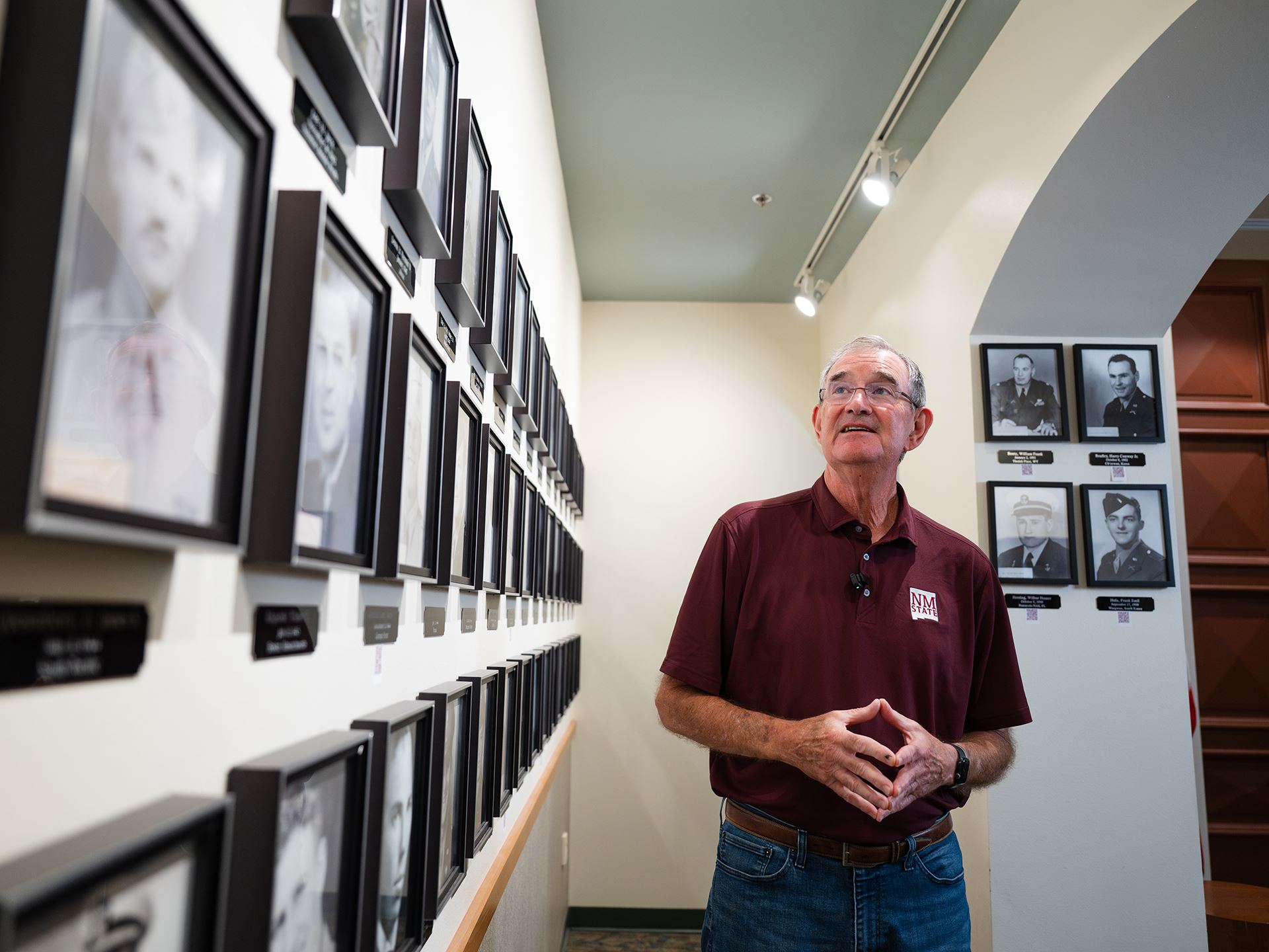 Photo of a man in an NMSU shirt and glasses looking at a display of black and white photos